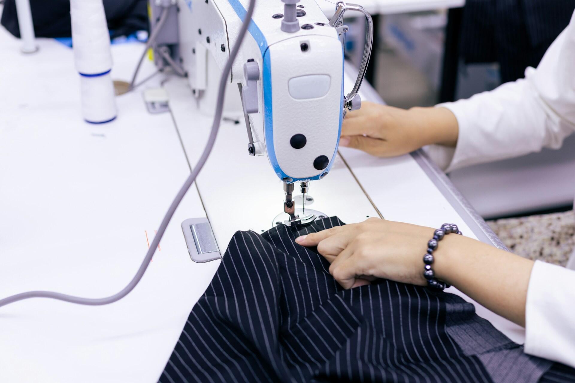 A person sewing a pinstriped garment on a sewing machine.