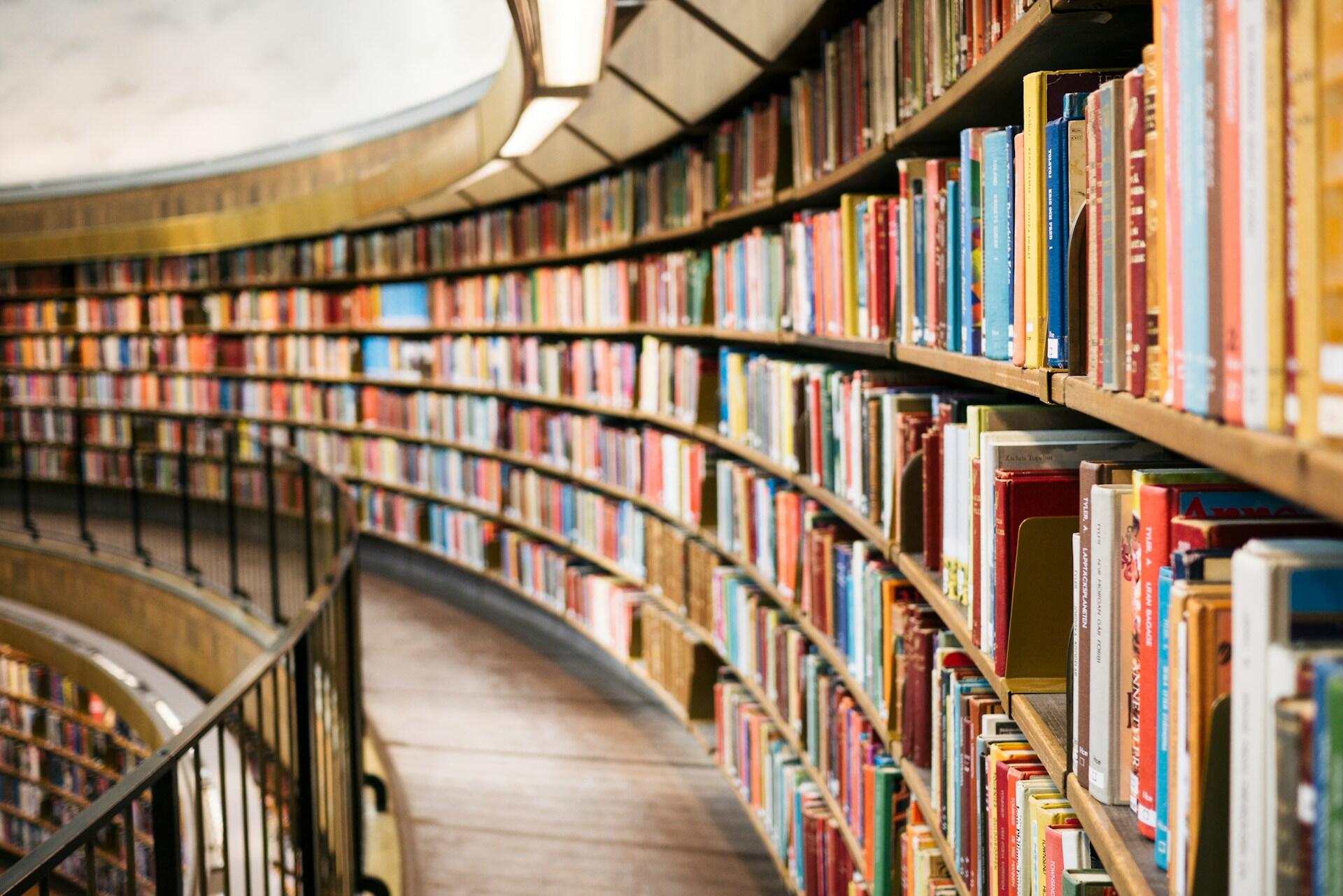 Curved library shelves filled with rows of books along a walkway with a railing.
