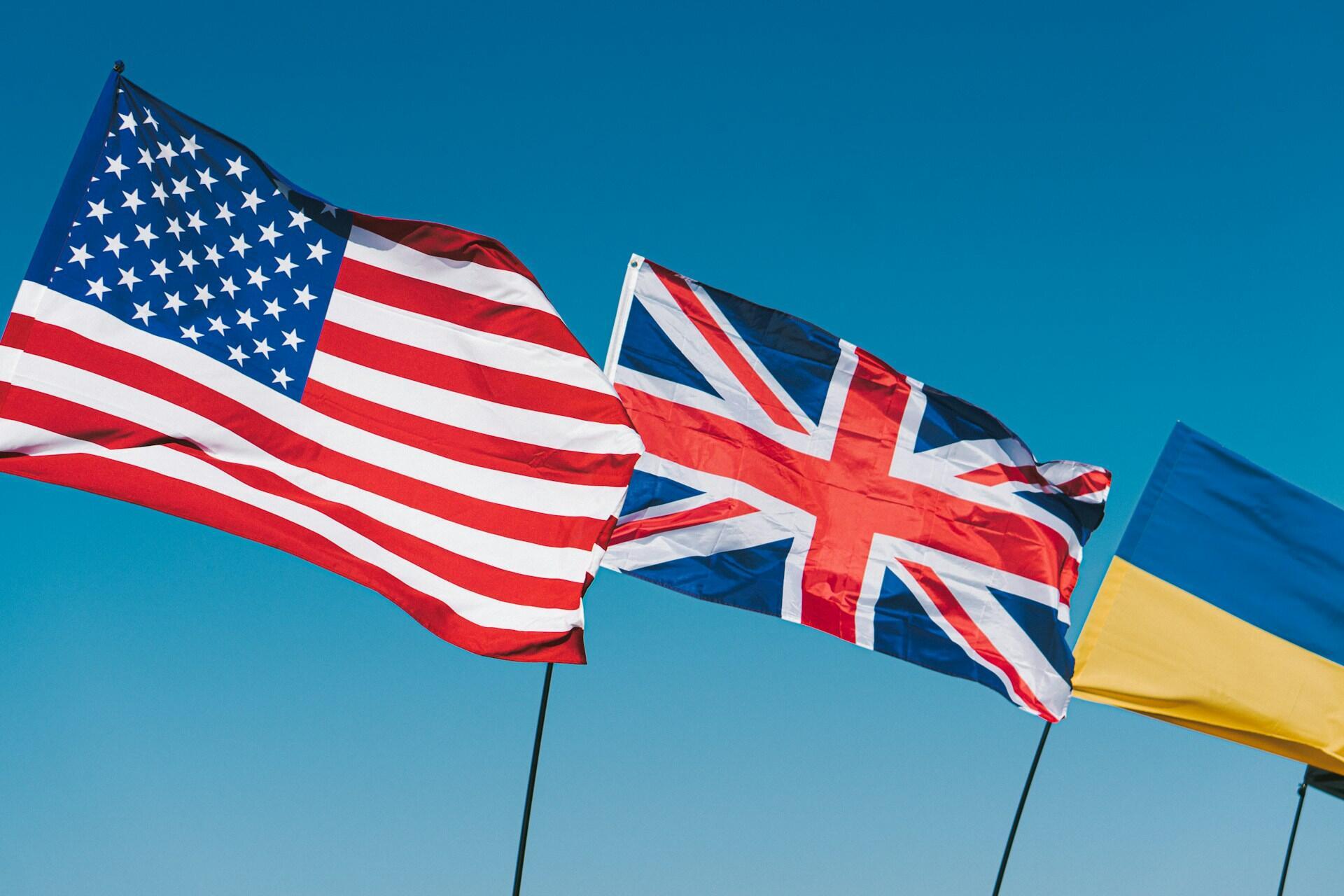 A British flag and an American flag fluttering side by side against a cloudless sky.