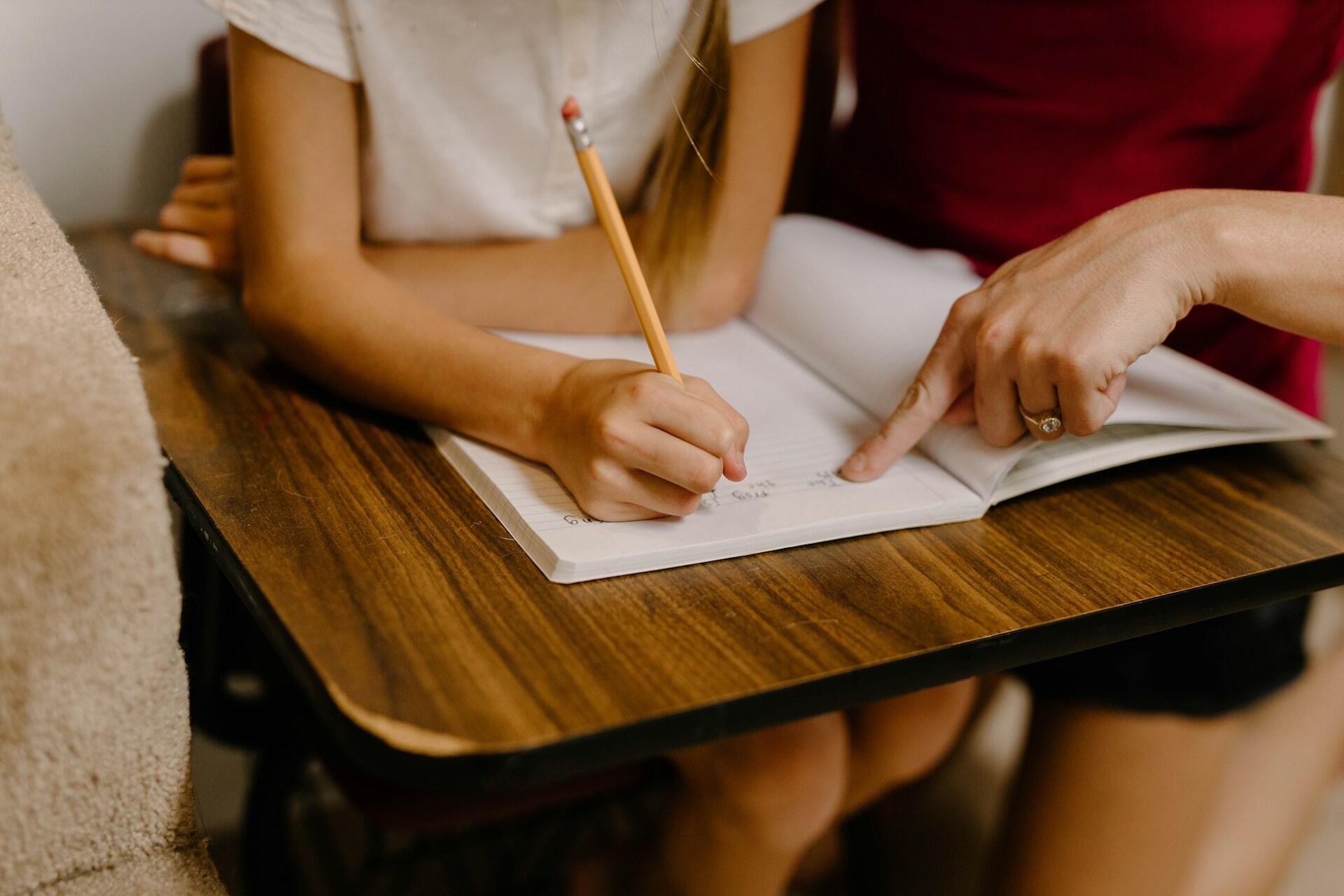 A tutor and a student sit together, writing in a notebook.