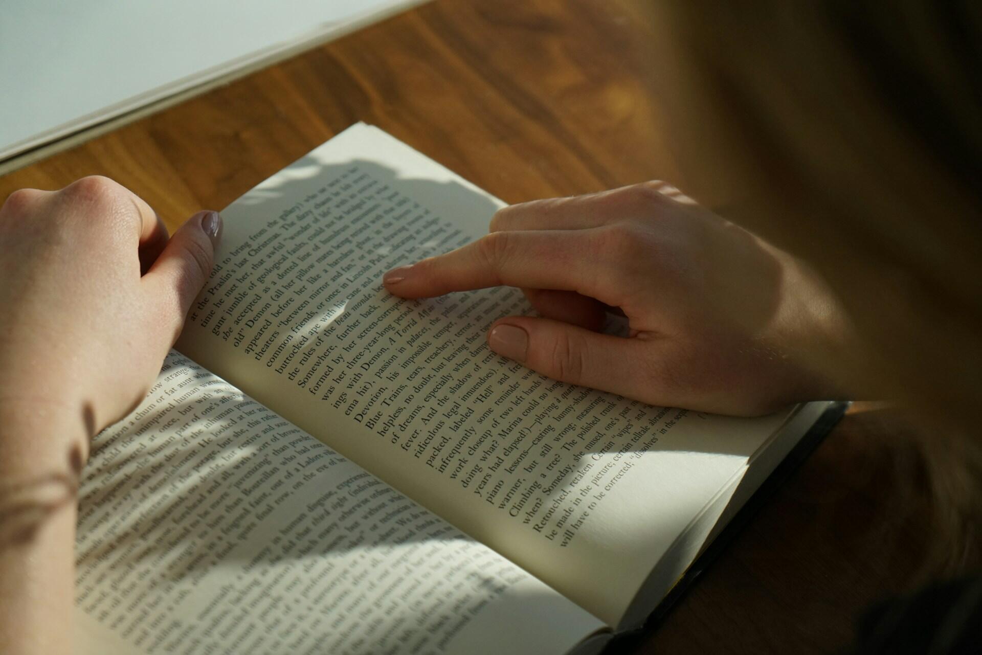 Person reading a book, pointing at text on a page.